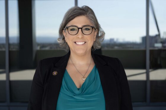 A professional woman with salt and pepper hair and glasses smiles at the camera.