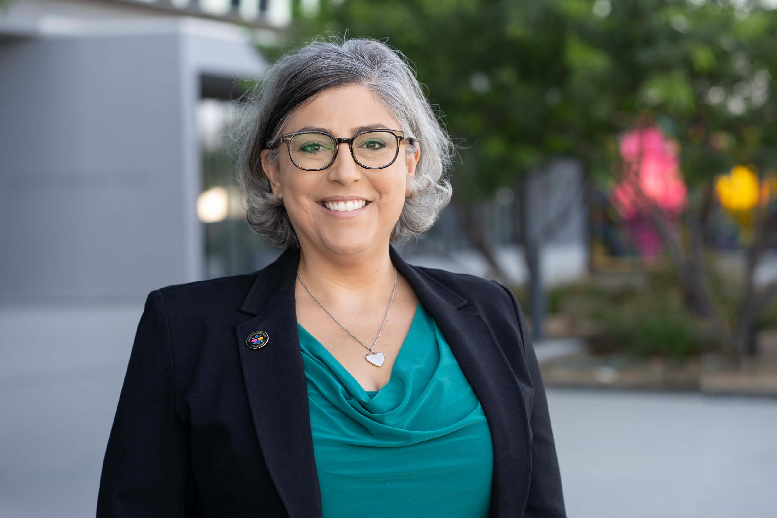 A woman with salt and pepper hair wearing glasses smiles at the camera.