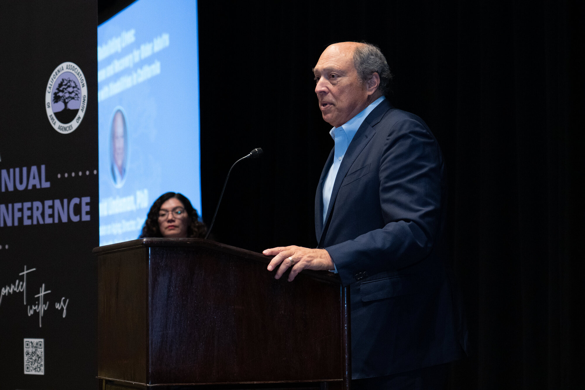 A man in a suit stands at a podium giving a speech.