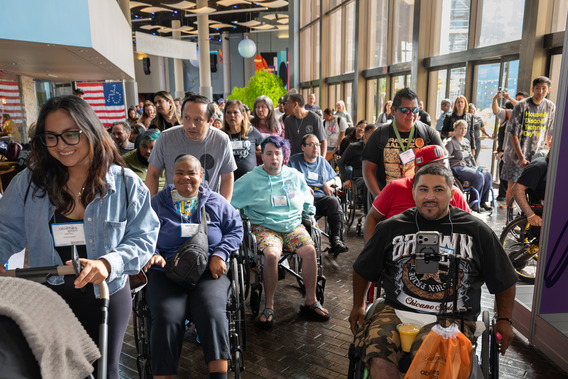 A group of diverse people, some using mobility devices, enter the Abilities Expo