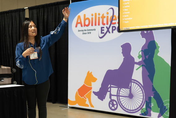 A woman gives a presentation in front of a sign for the Abilities Expo