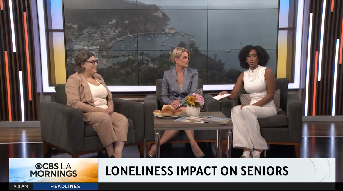 Three women sit on a news show set in discussion with a chyron at the bottom that says "Loneliness Impact on Seniors"