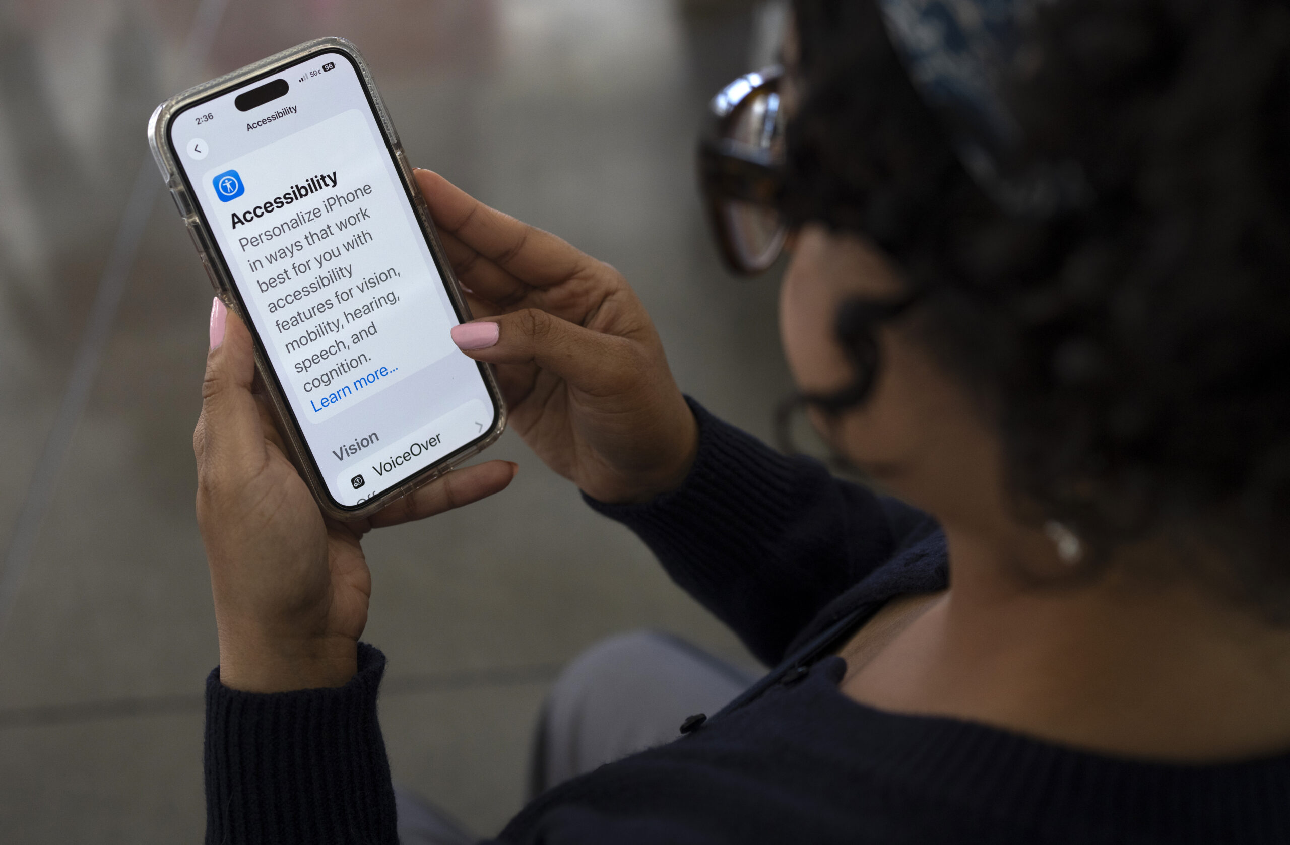 A woman holds a phone which displays the accessibility settings phone screen.